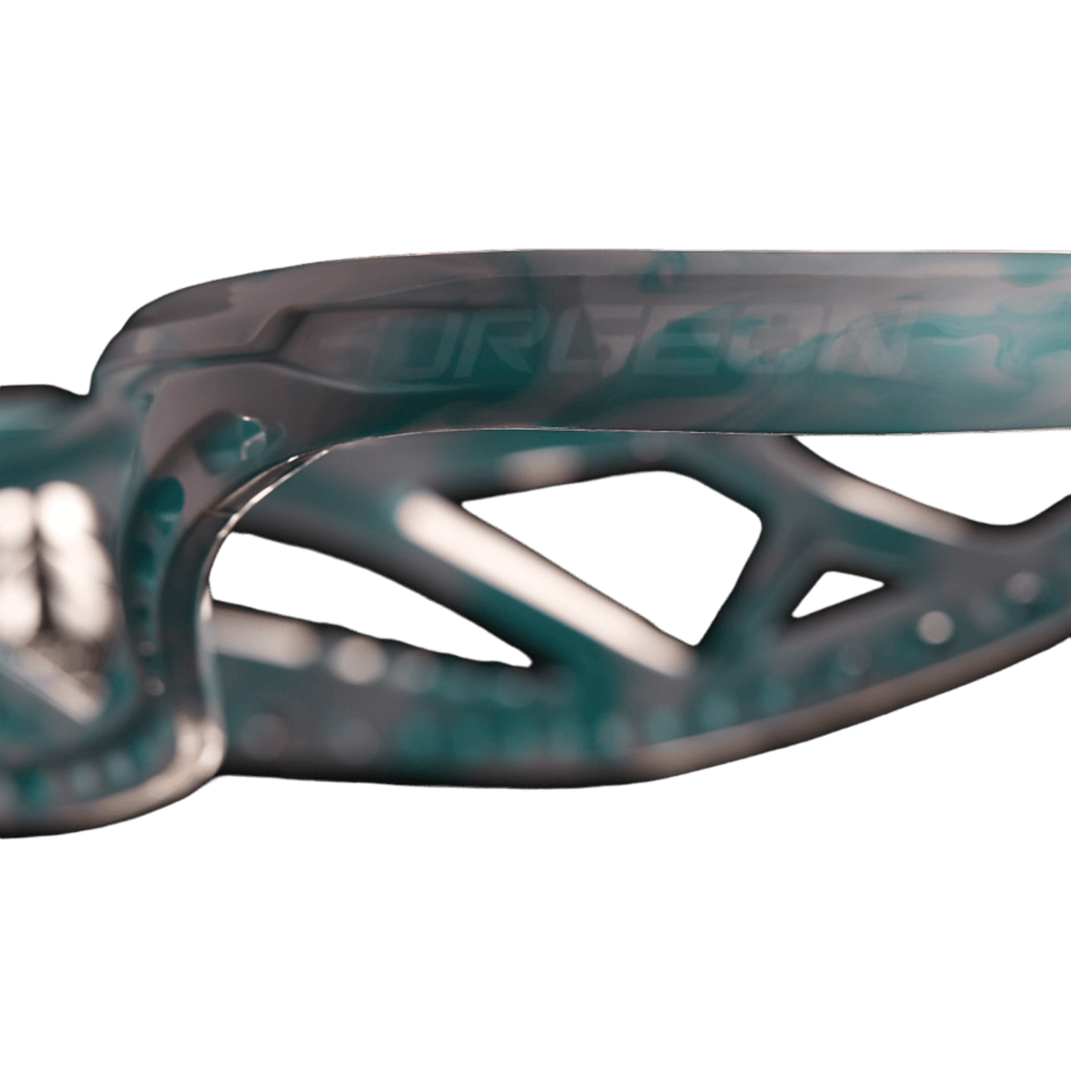 Close-up of the STX Surgeon 900 Lacrosse Head, showcasing a lightweight design with a metallic geometric aesthetic. The translucent object features teal and gray shades, highlighted by intricate patterns and cut-out sections.